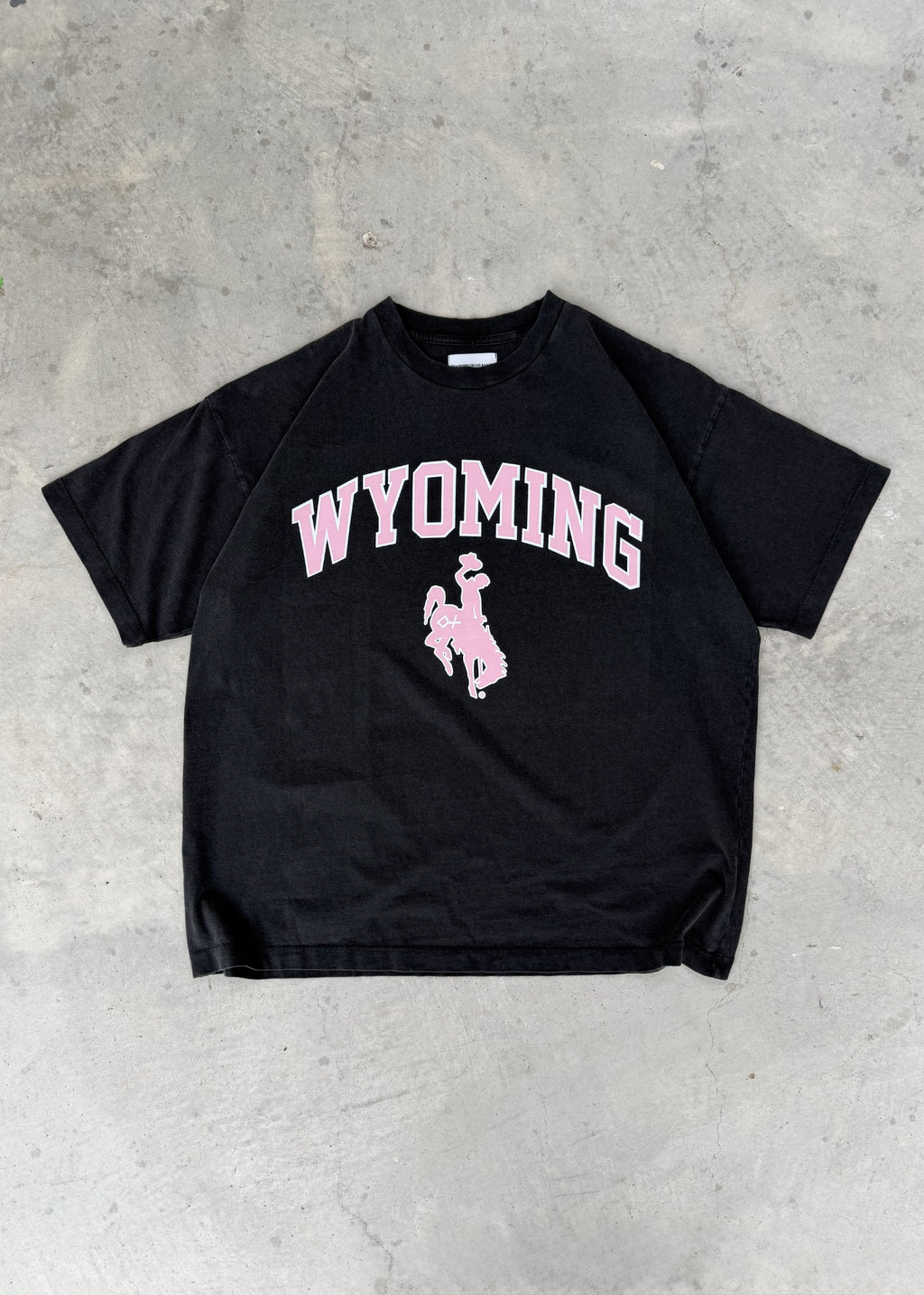 Faded Black + Rose | Black t-shirt with 'Wyoming' printed in pink on a concrete floor