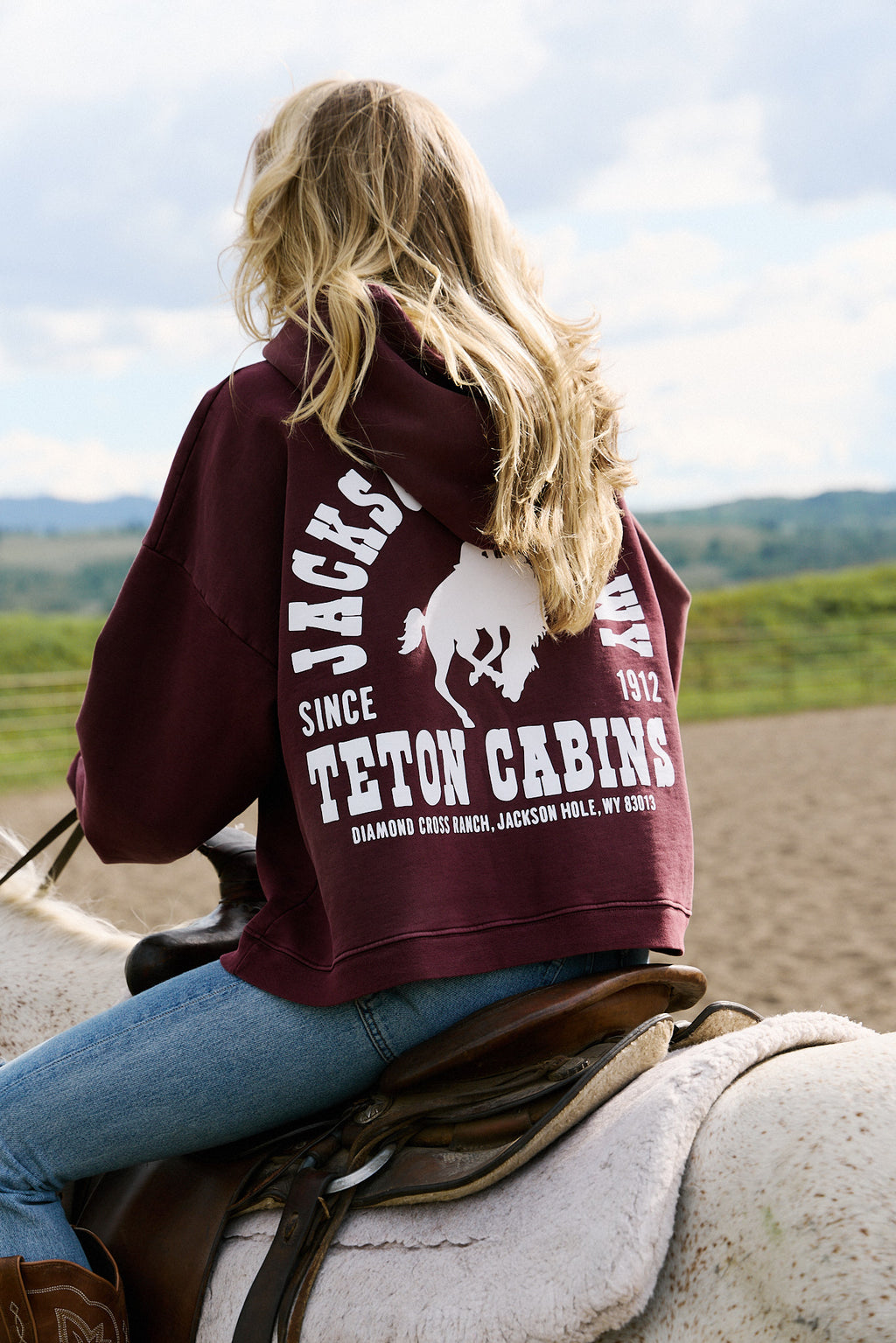 Burgundy | Person wearing a maroon hoodie with 'Teton Cabins' branding, sitting on a horse.