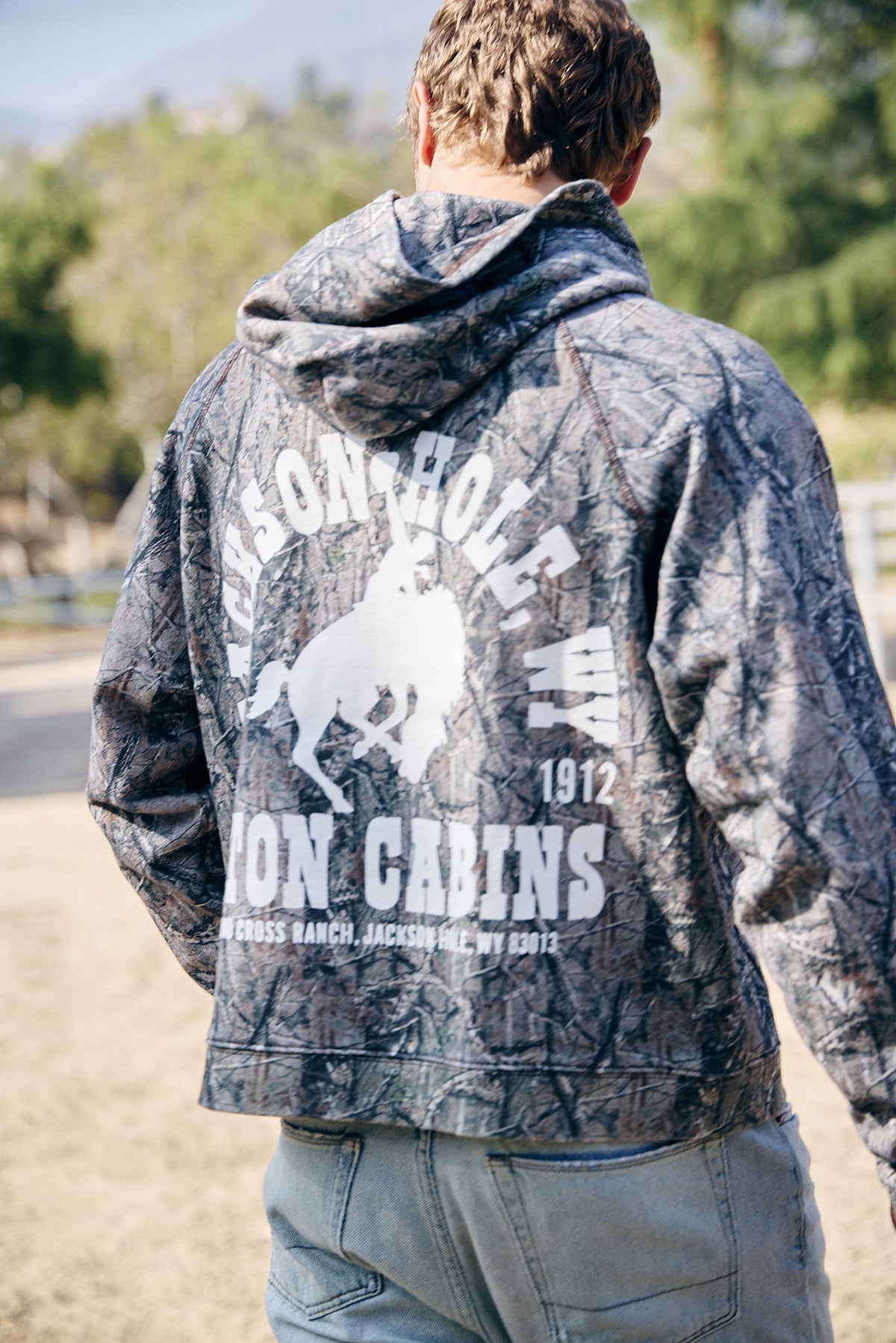 Sage Brush Camo | Person wearing a hoodie with branding on the back, standing outdoors.