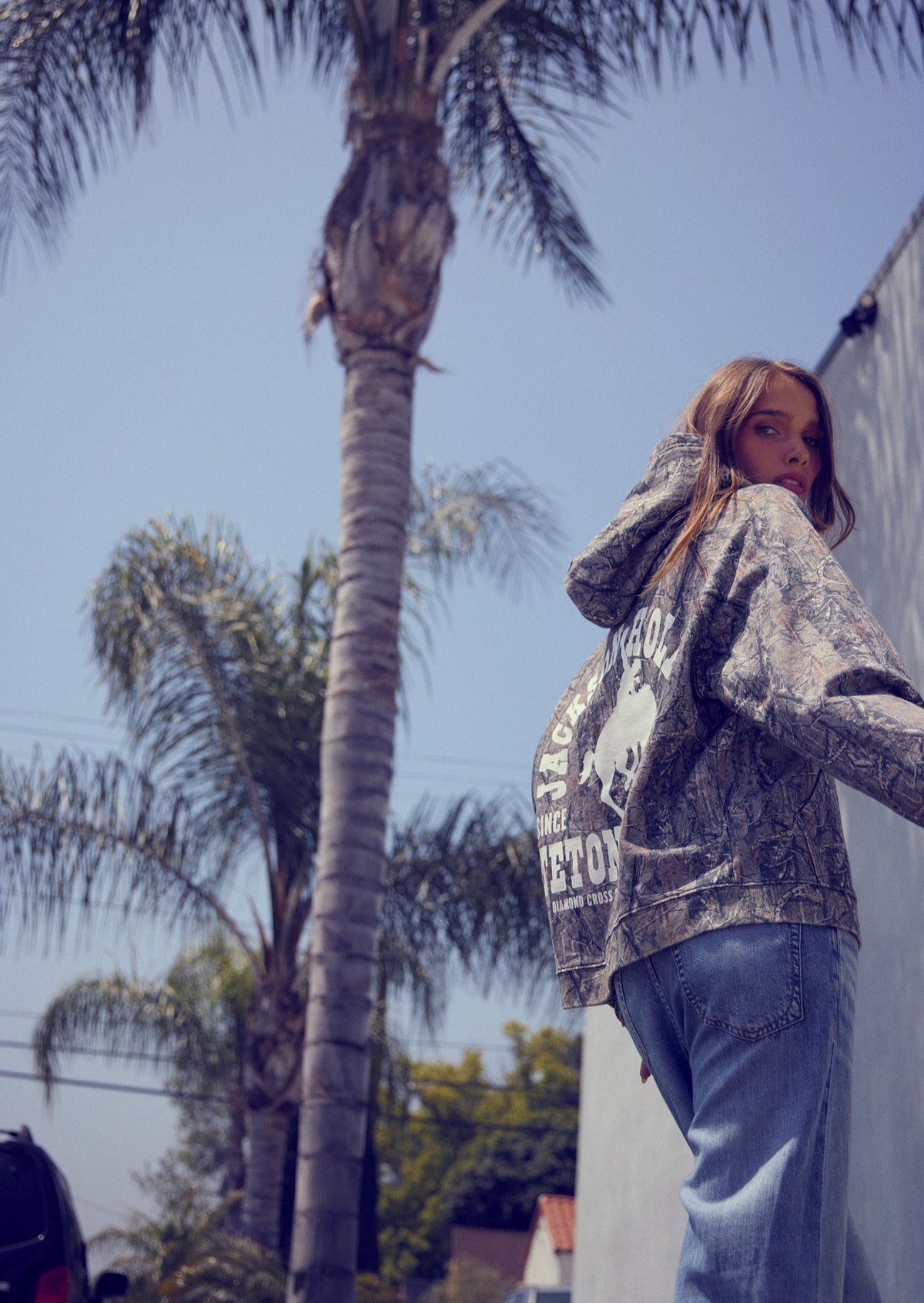 Sage Brush Camo | Person wearing a hoodie with text and graphics outdoors with palm trees in the background