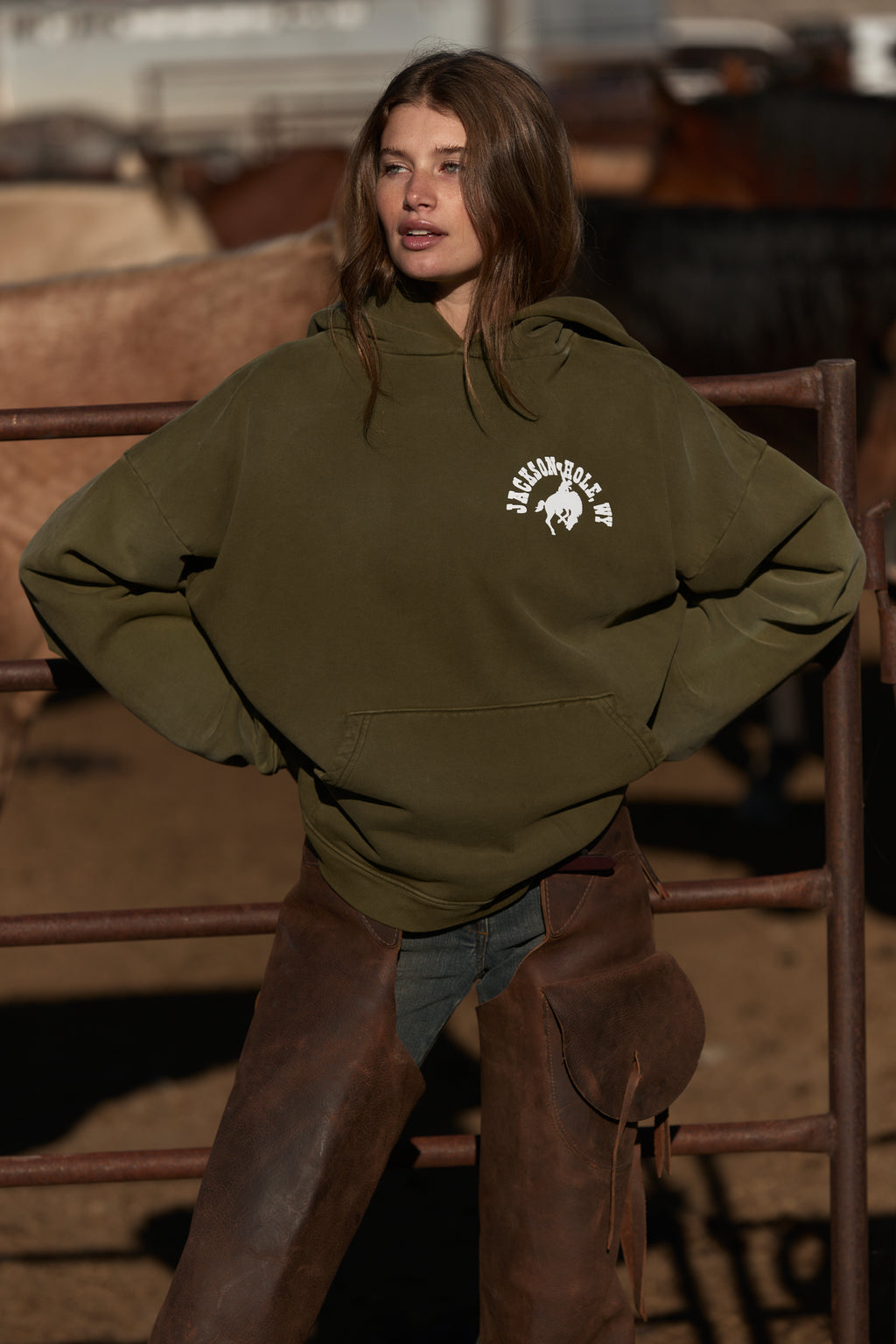 Army Green | Person wearing an olive green hoodie with a logo, standing in front of a rustic background.