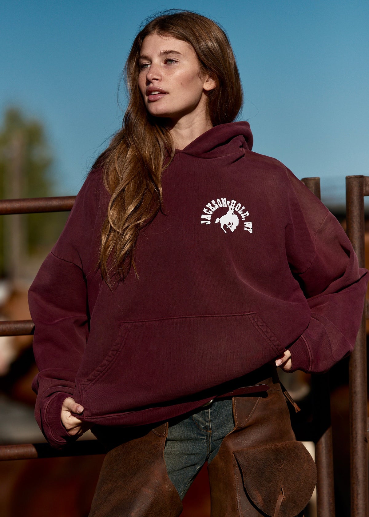 Burgundy | Woman wearing a burgundy hoodie with a logo, standing outdoors.