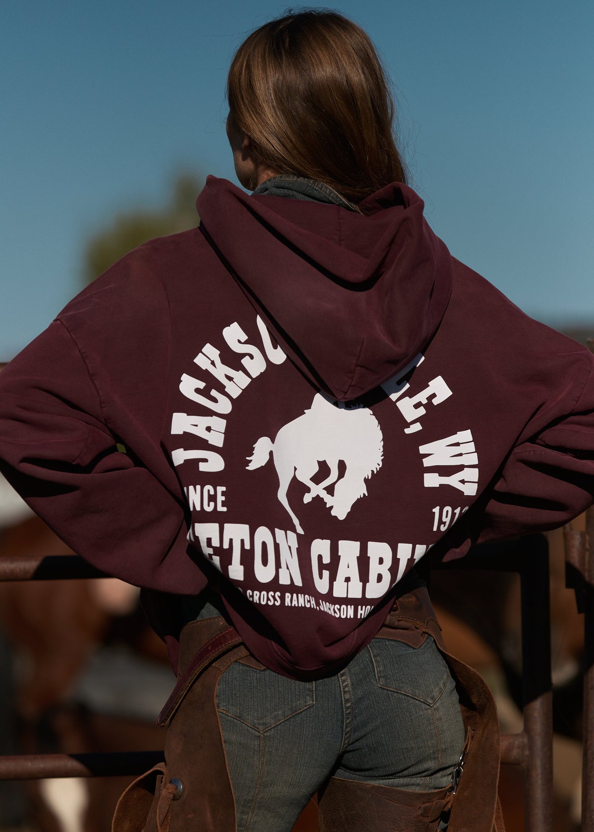 Burgundy | Person wearing a maroon hoodie with branding, standing outdoors.
