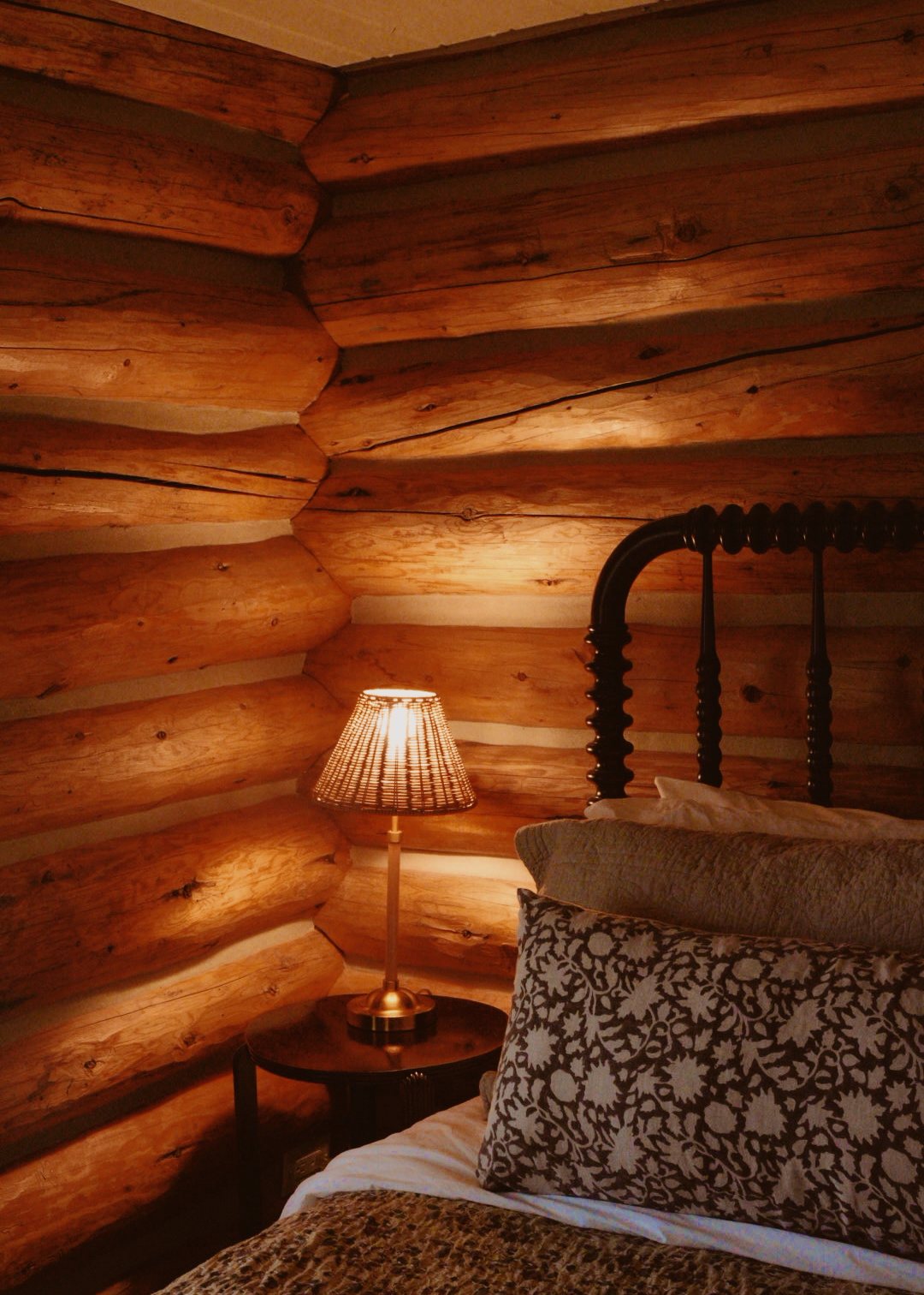 Bedroom with log walls and an iron bed in a renovated Teton Cabin