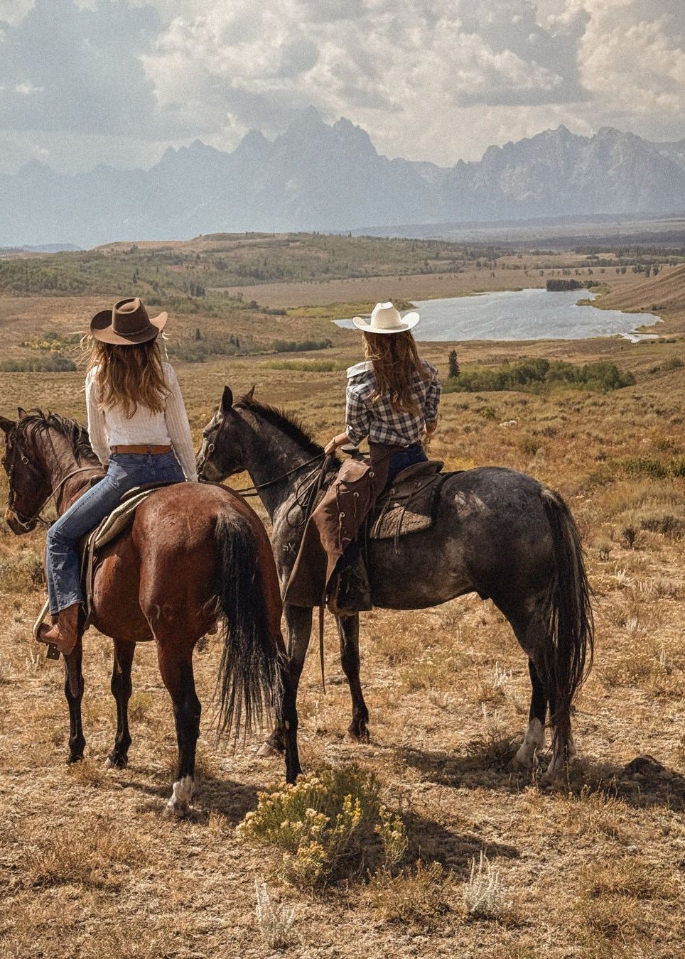 Two riders on horseback overlooking the valley and the Tetons