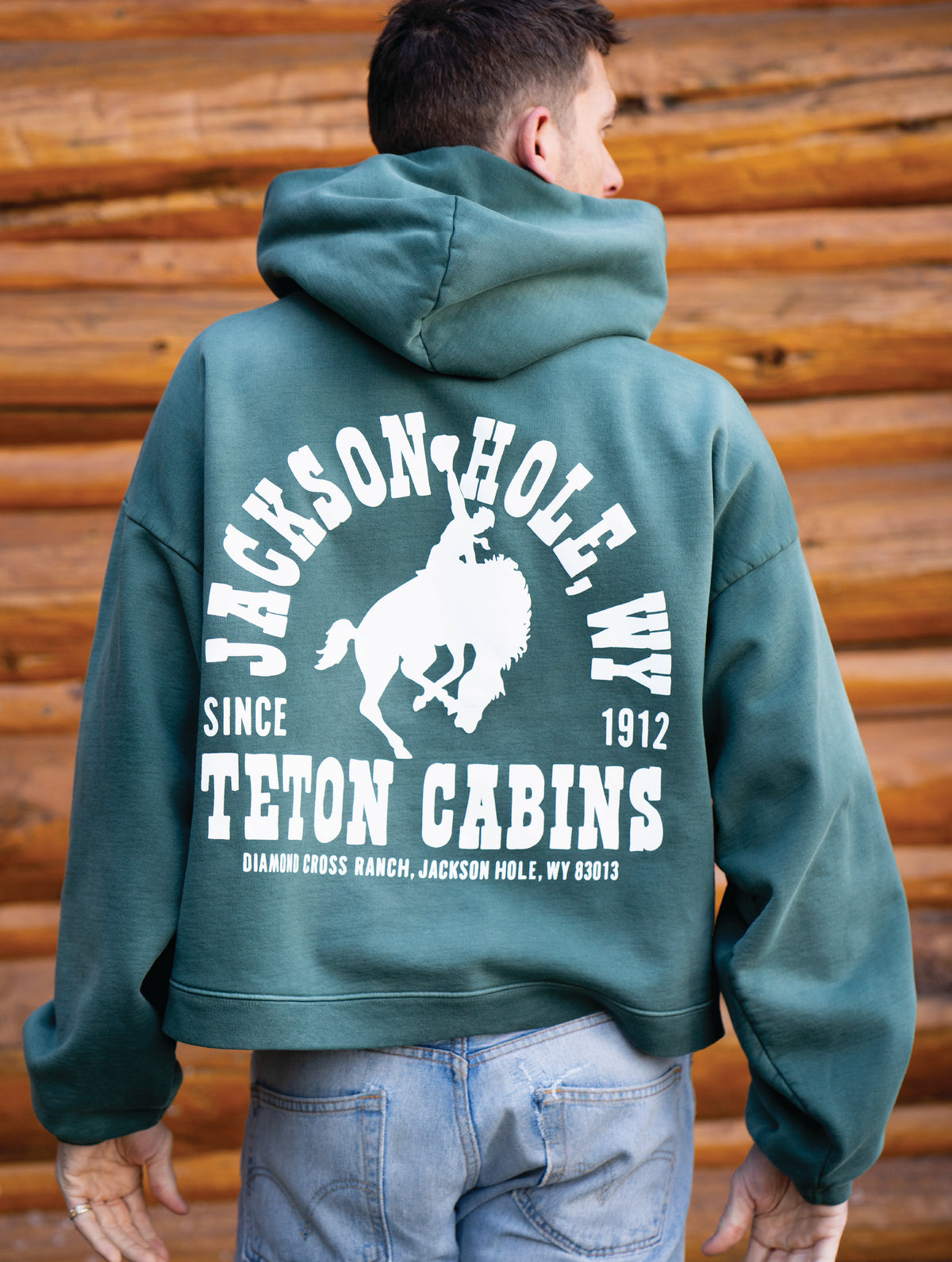 Sun Faded Green | Person wearing a green hoodie with 'Jackson Hole, WY' text and logo against a wooden background
